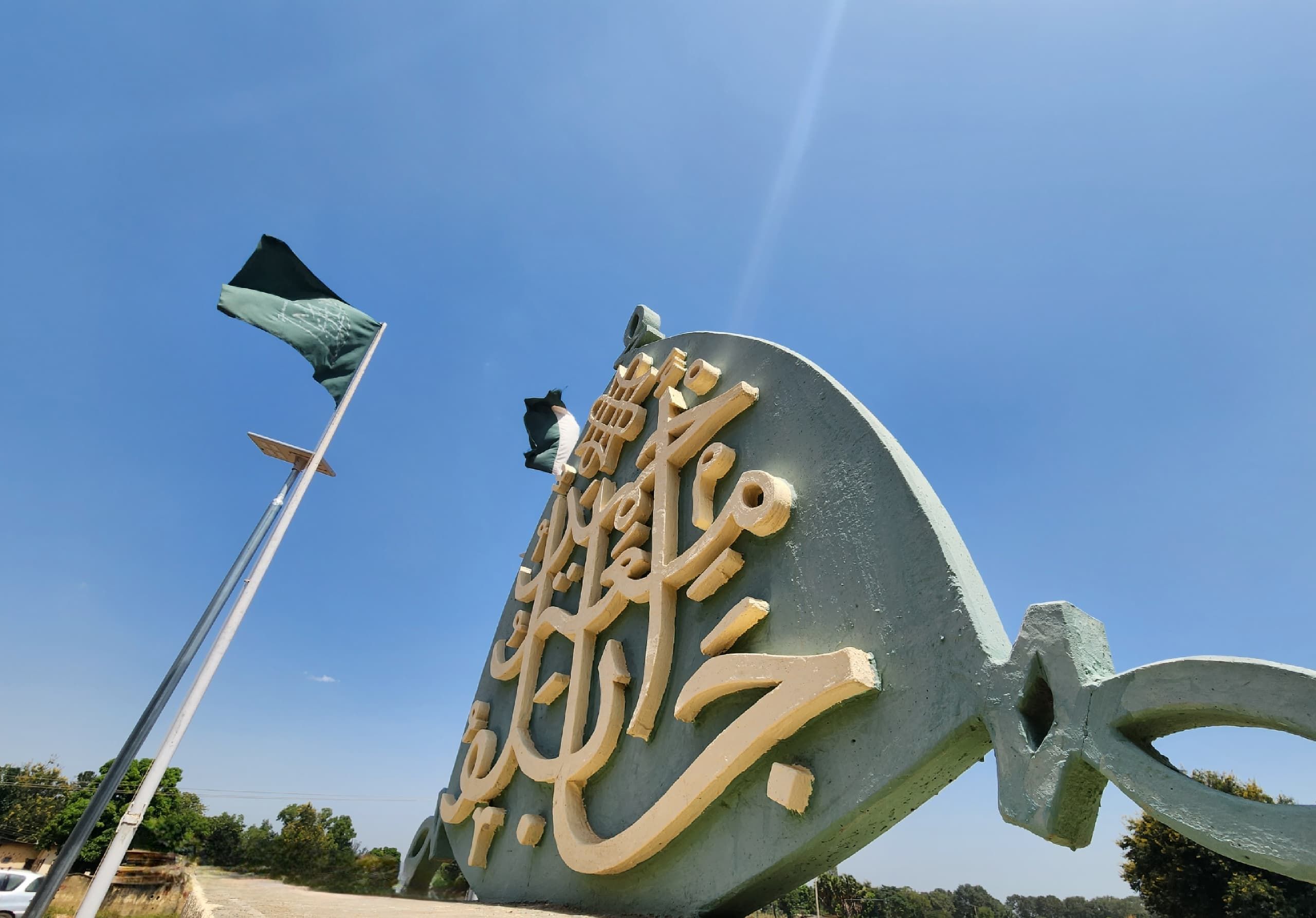 The calligraphic crest monument at the entrance of Ahmadu Bello University, with green university flags flying